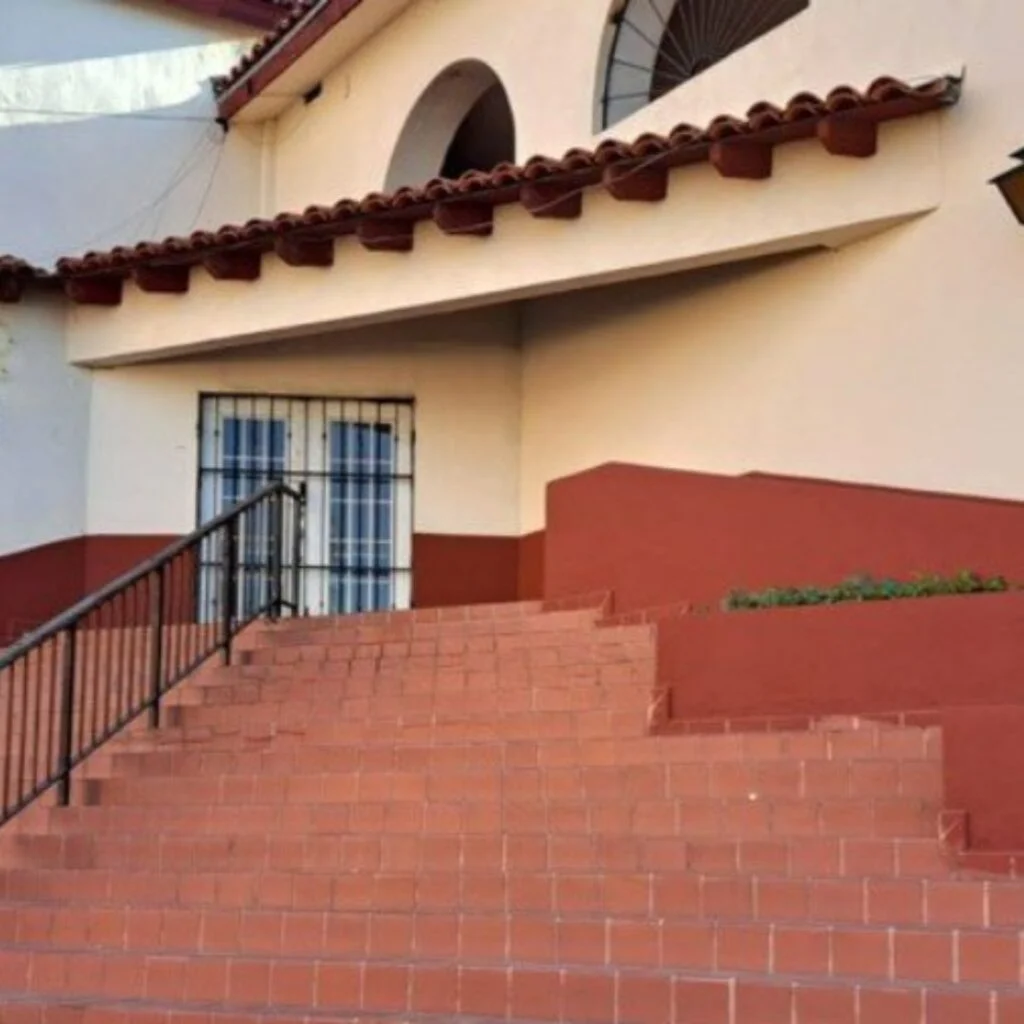 A red, wide brick staircase leading up to a cream and red Spanish architecture building.